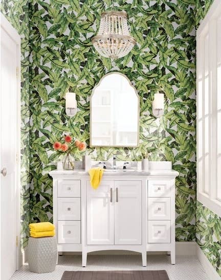 green palm leaf wallpaper on a bathroom wall behind a mirror and white sink