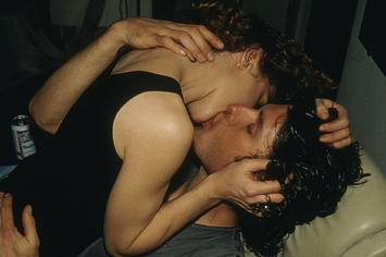 Two young people in jeans passionately kissing on a white leather chair