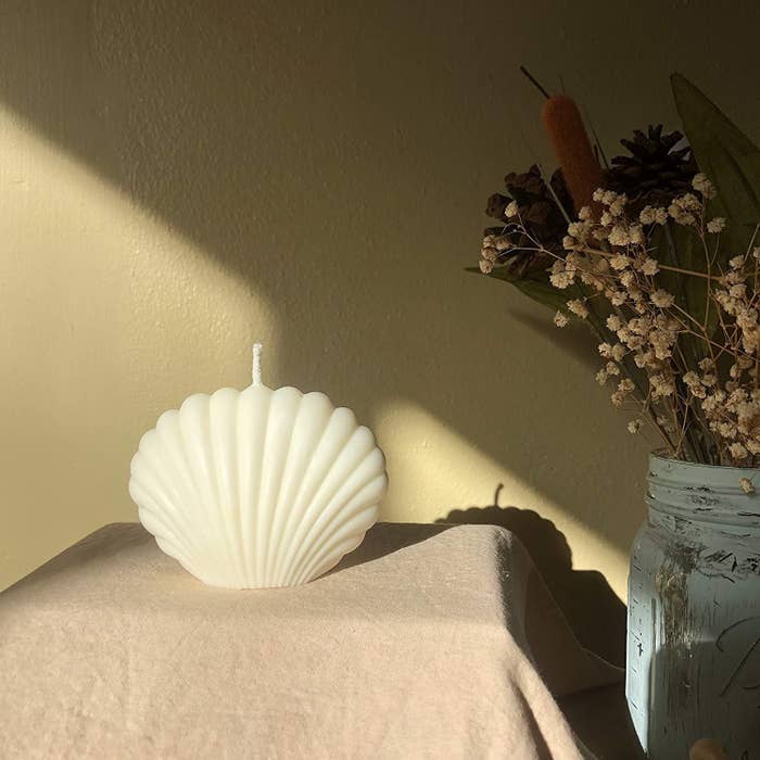 white seashell candle styled next to some flowers in a vase
