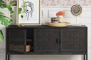 The rattan TV stand in black holding a framed drawing and a wicker basket