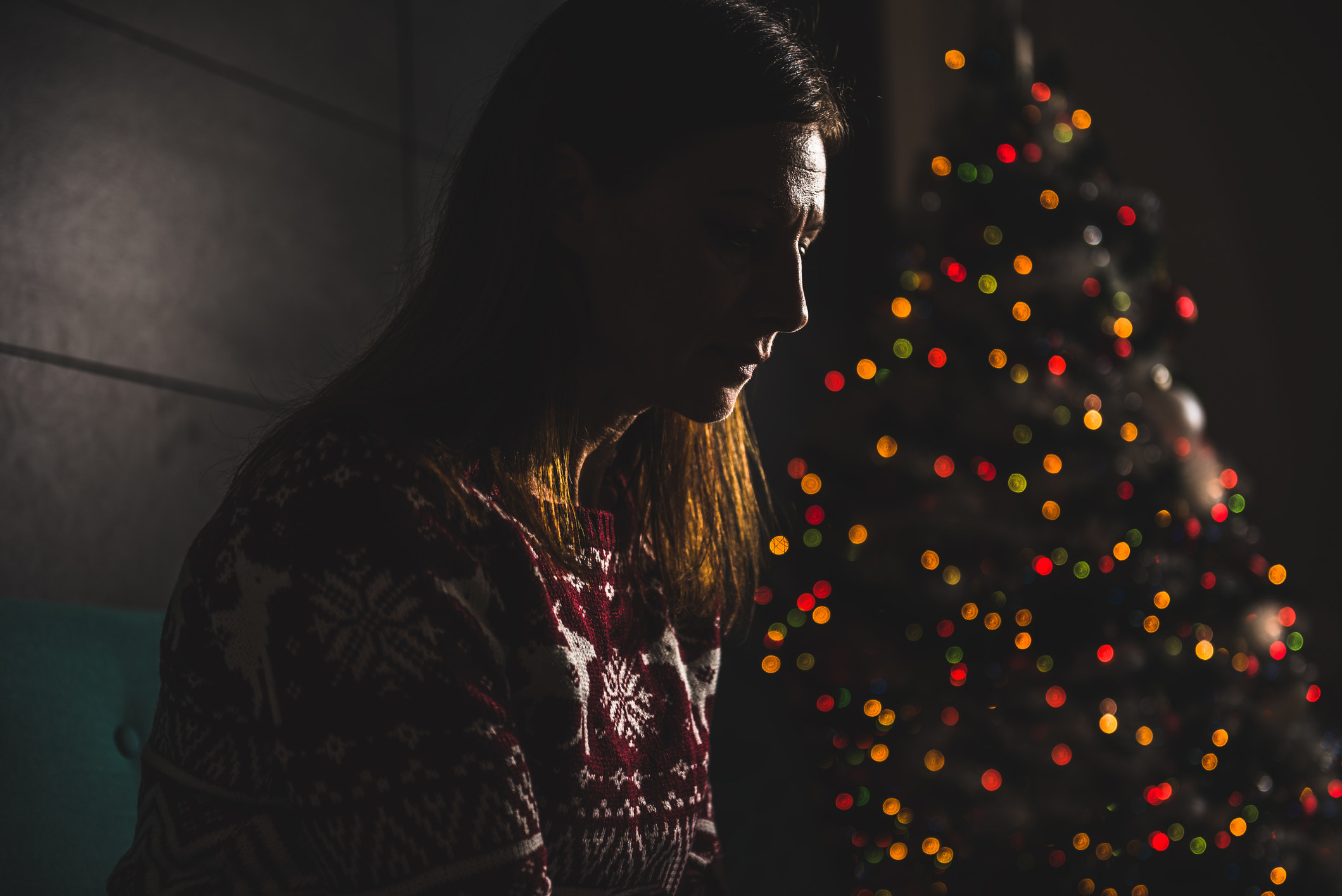Someone looks devastated while sitting alone in the dark next to a Christmas tree