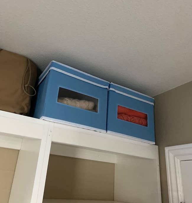 Two light blue fabric storage boxes on top of a closet