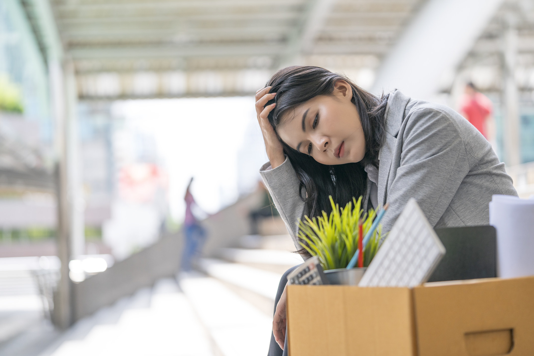 An employee sitting with a box of office supplies, as if leaving a job