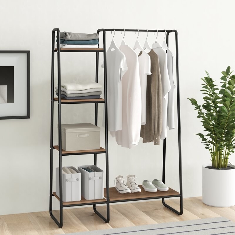 open garment rack with black frame and wood shelves, with clothes and accessories on the shelves and hanging on the top rack