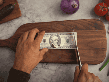 Someone cutting up money on a cutting board like it&#x27;s a carrot