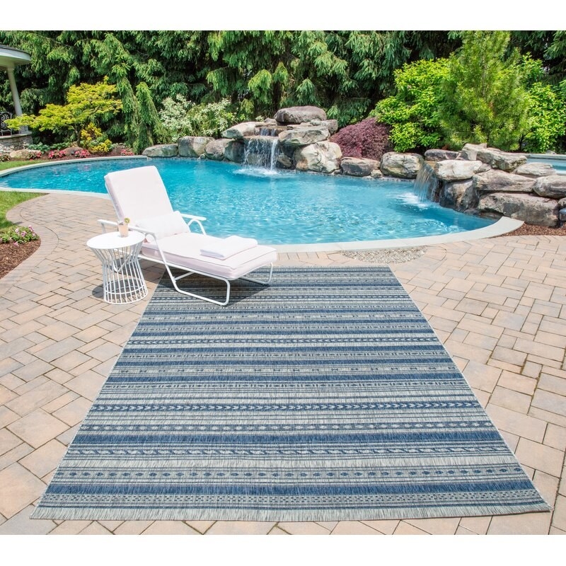 blue and white striped rug outdoor under a lounge chair and next to a swimming pool