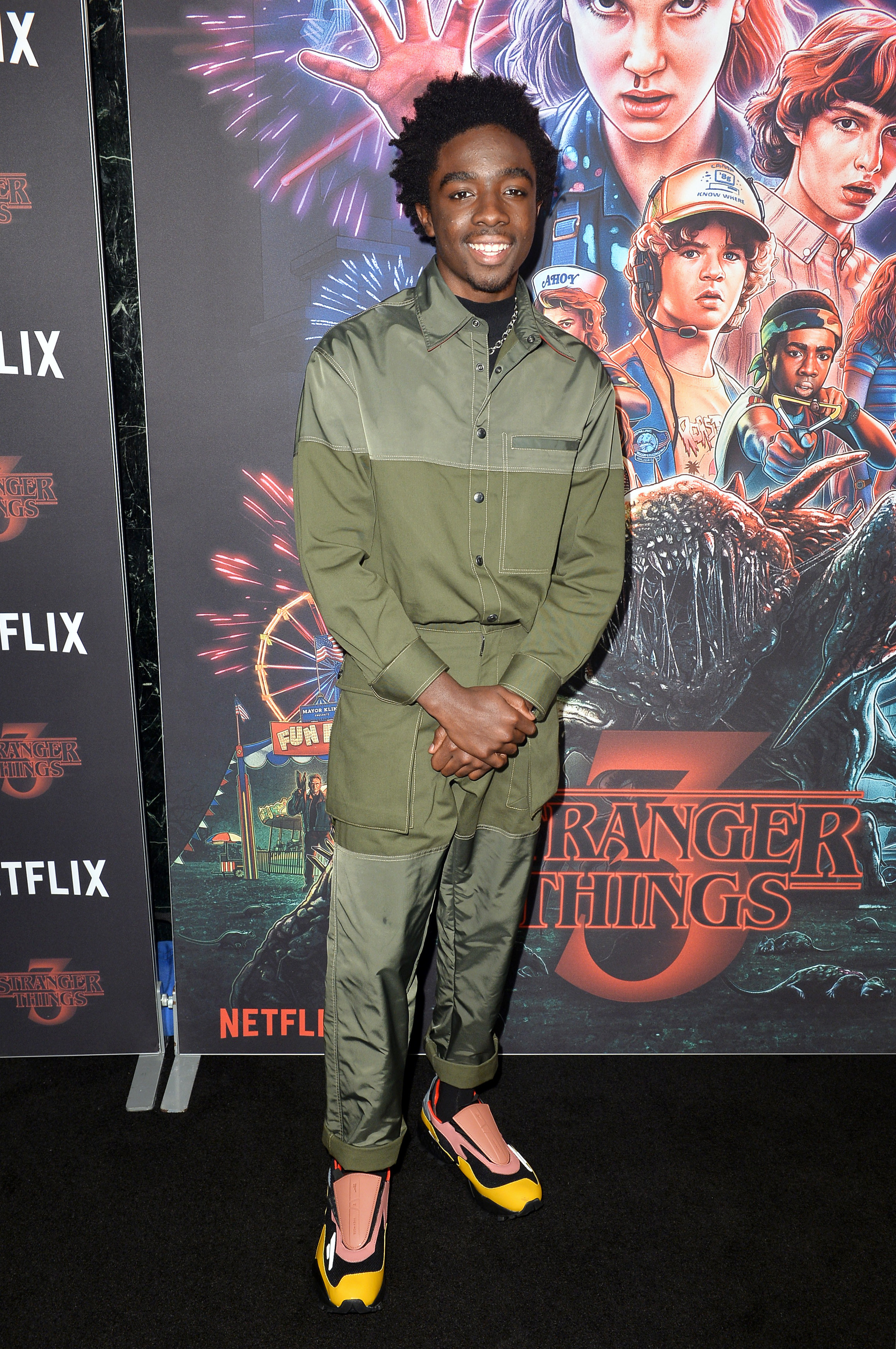 Caleb is smiling at a premiere wearing another monochromatic outfit with multicolored sneakers. 