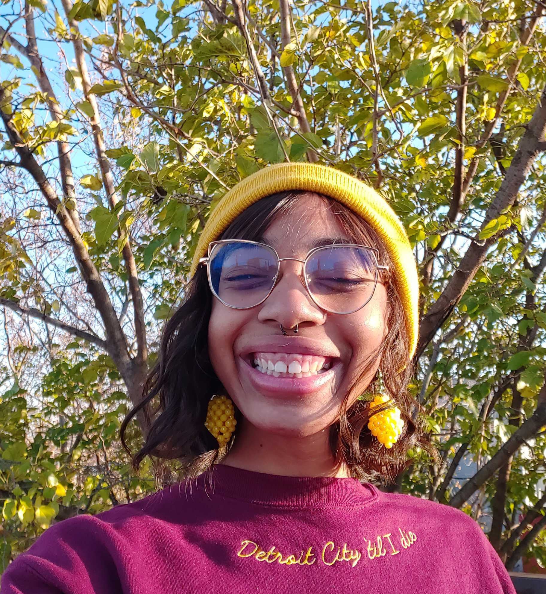 buzzfeeder in a maroon crewneck sweatshirt with &quot;detroit city &#x27;til I die&quot; embroidered in mustard along the neckline