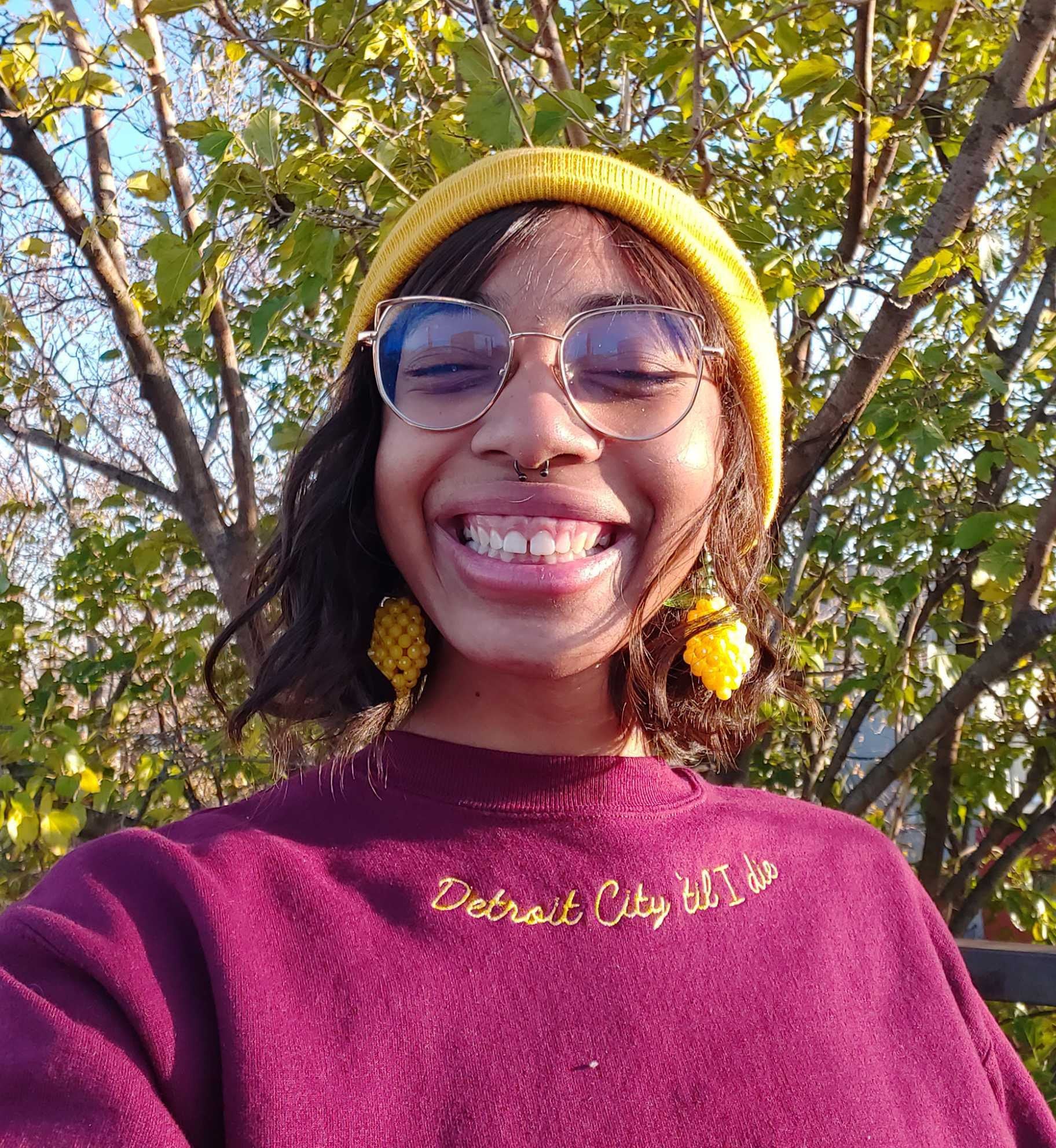 buzzfeeder in a maroon crewneck sweatshirt with &quot;detroit city &#x27;til I die&quot; embroidered in mustard along the neckline