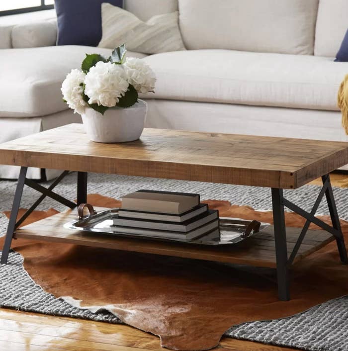 The coffee table with storage in natural pine brown holding a tray of books and flowers