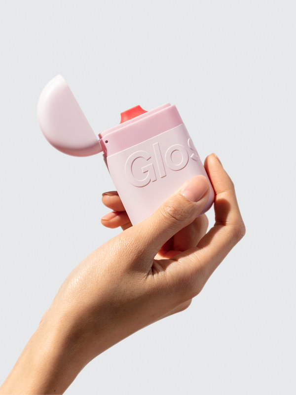 a model&#x27;s hand holds up the glossier hand cream container