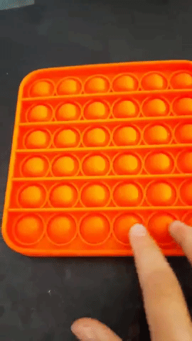 reviewer popping tiny semi-circles in an orange silicone fidget toy 