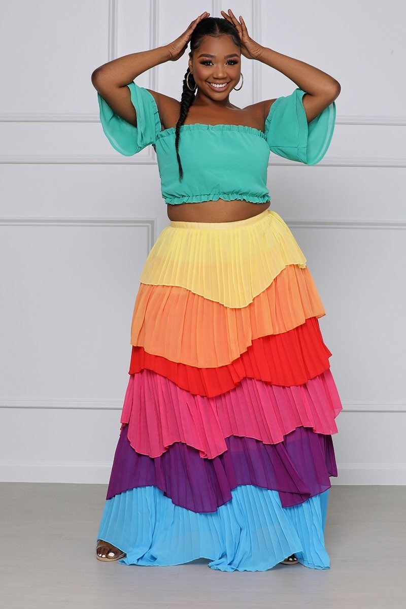 a model wearing a green off the shoulder top with a layered rainbow maxi skirt