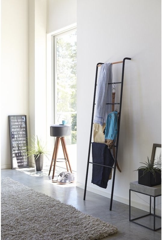 Black blanket ladder propped up against a wall with accessories hung on it