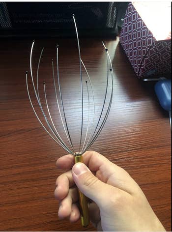 Reviewer holding up the scalp tingler  with multiple flexible wires attached to the handle 