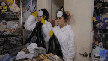 Abbi and Ilana wearing masks and gloves while holding garbage bags getting motivated to deep clean
