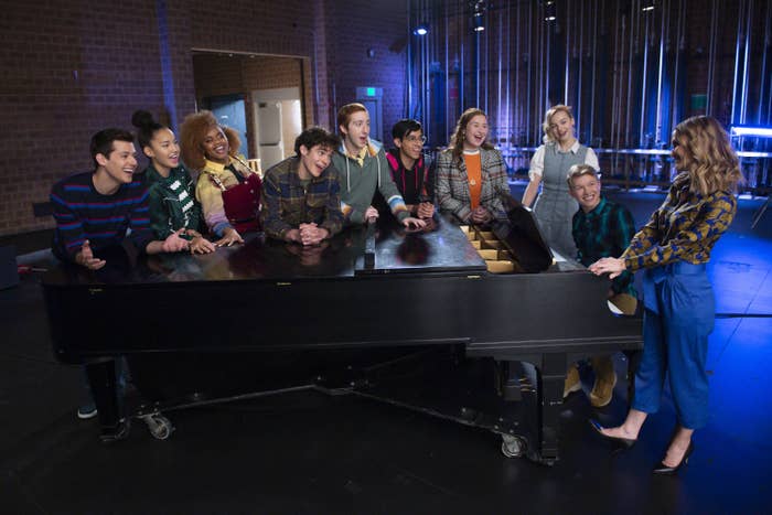 The cast standing around a piano
