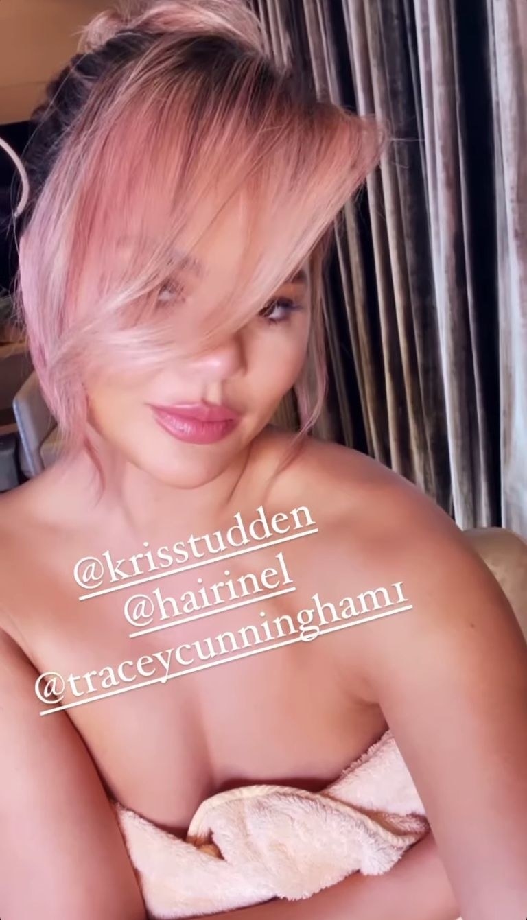 Chrissy has pink hair pulled back in a bun with dramatic side swept bangs