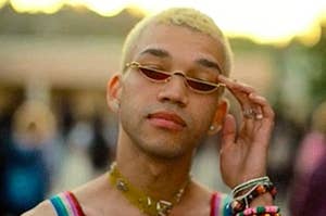 A fashionably dressed teenager lowers the lenses on his sunglasses as he addresses someone.
