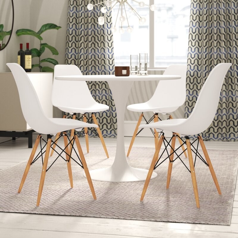 four white plastic chairs with wood legs around a round table