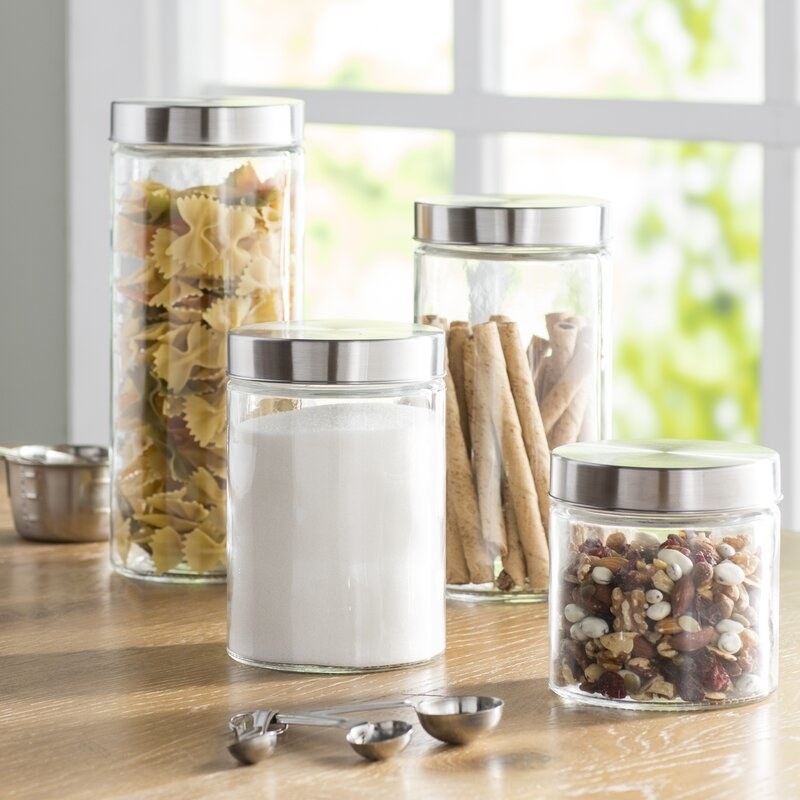 set of four glass canisters of different heights with stainless steel tops, filled with arious dry goods