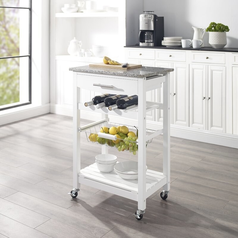 white kitchen cart with white rack, metal basket, wheels, and granite top