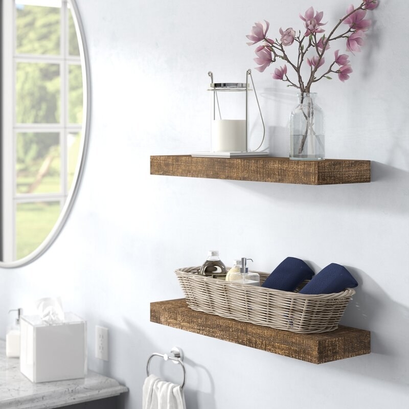 two wood floating shelves in a bathroom with accessories on top
