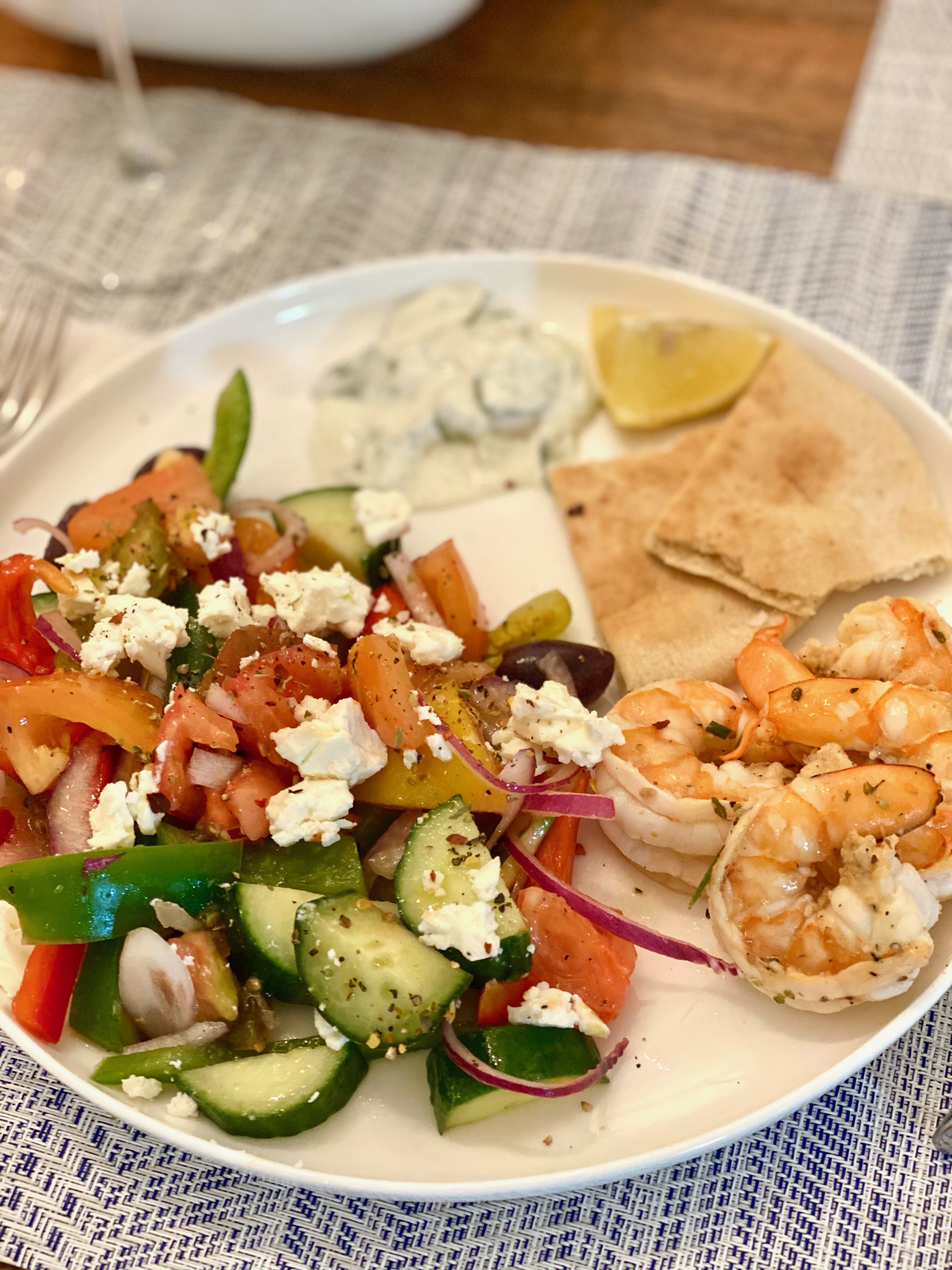 A traditional Greek salad with pita and grilled shrimp on the side.