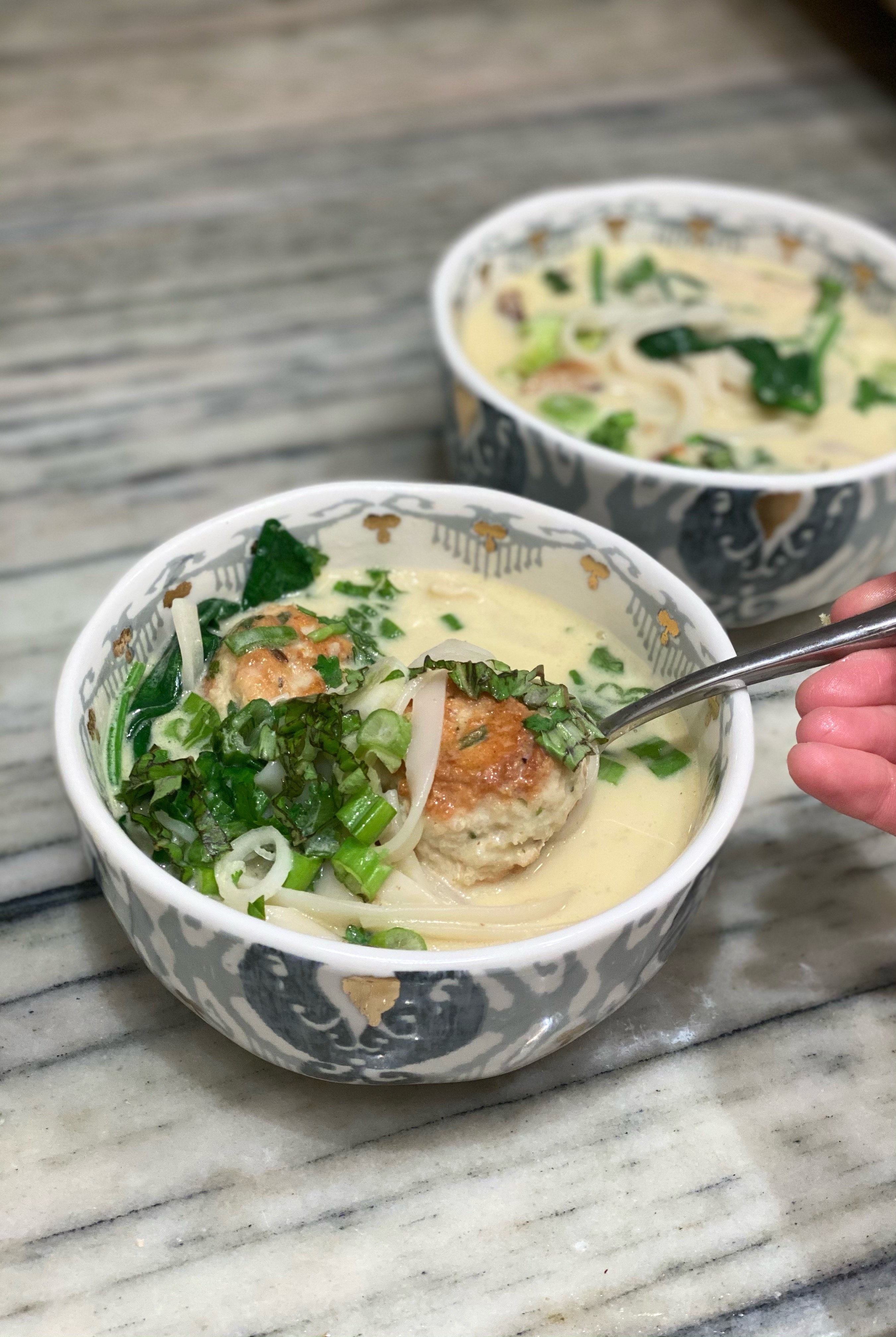 A bowl of meatballs and rice noodles in coconut broth.