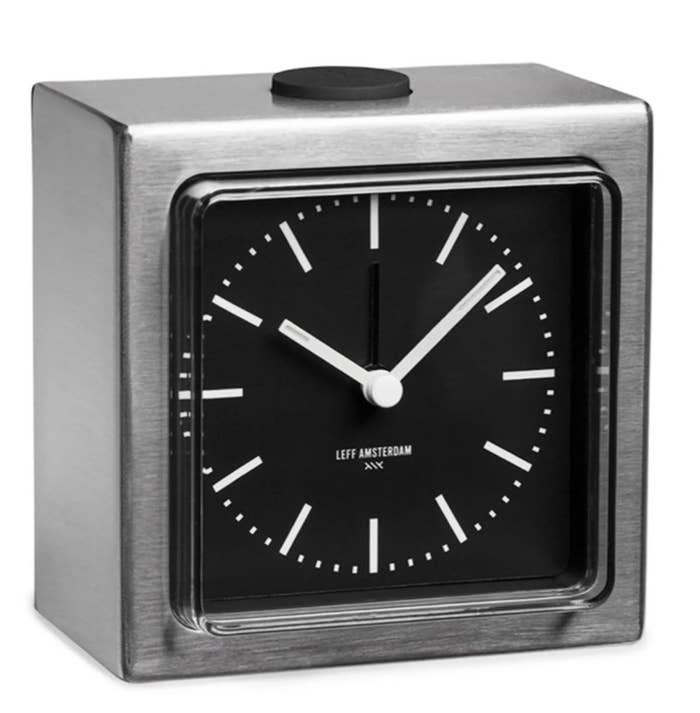 a silver block alarm clock with white arms and a black clock face