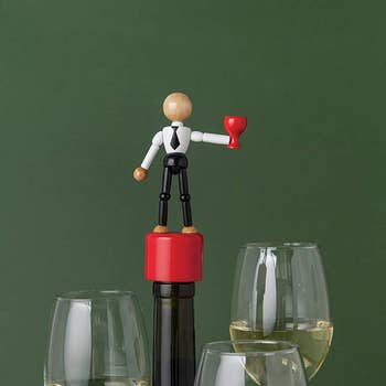 red bottle stopper with a figure of a person in black pants, a white shirt, and a black tie holding a red wine glass