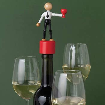 red bottle stopper with a figure of a person in black pants, a white shirt, and a black tie holding a red wine glass