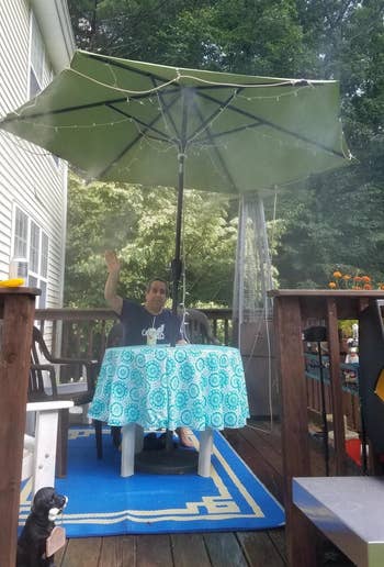a reviewer sits connected their patio nether an umbrella with the orbit outdoor mist cooling strategy attached to it and spraying mist