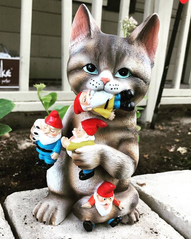 statue of tabby cat grabbing and eating small gnomes
