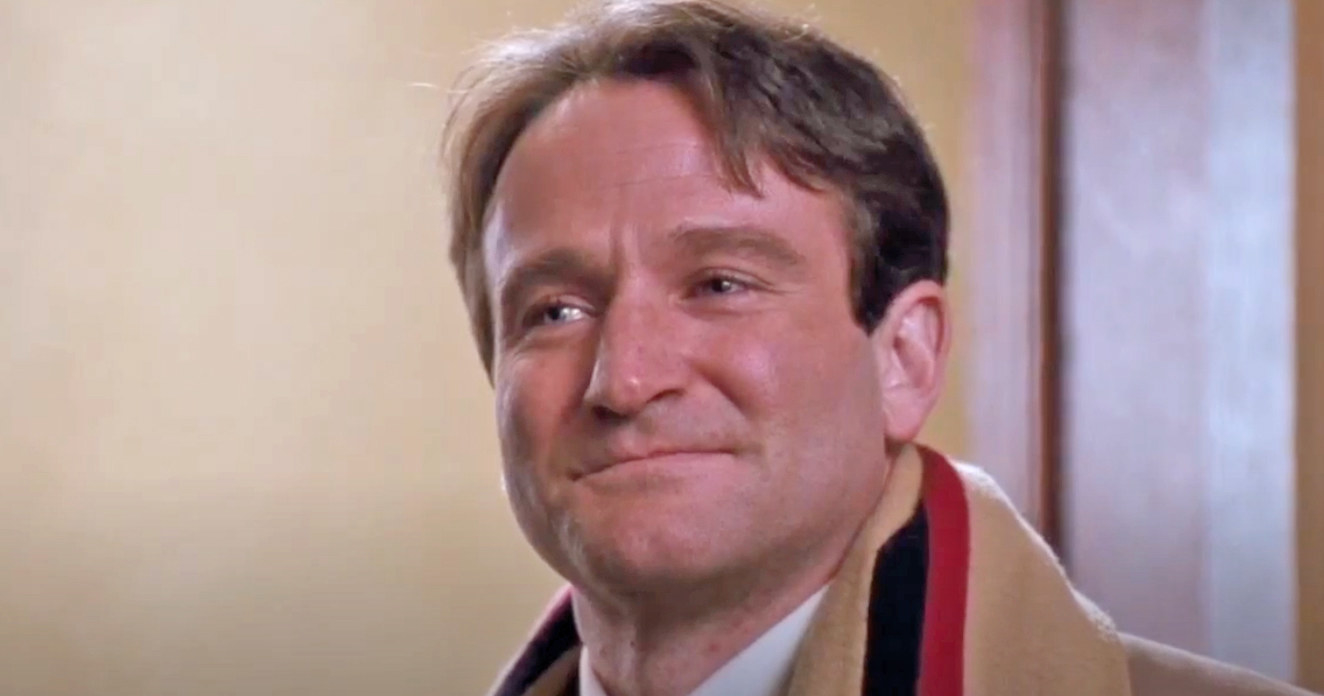 Robin Williams smiles softly while standing in a doorway as Mr. Keating