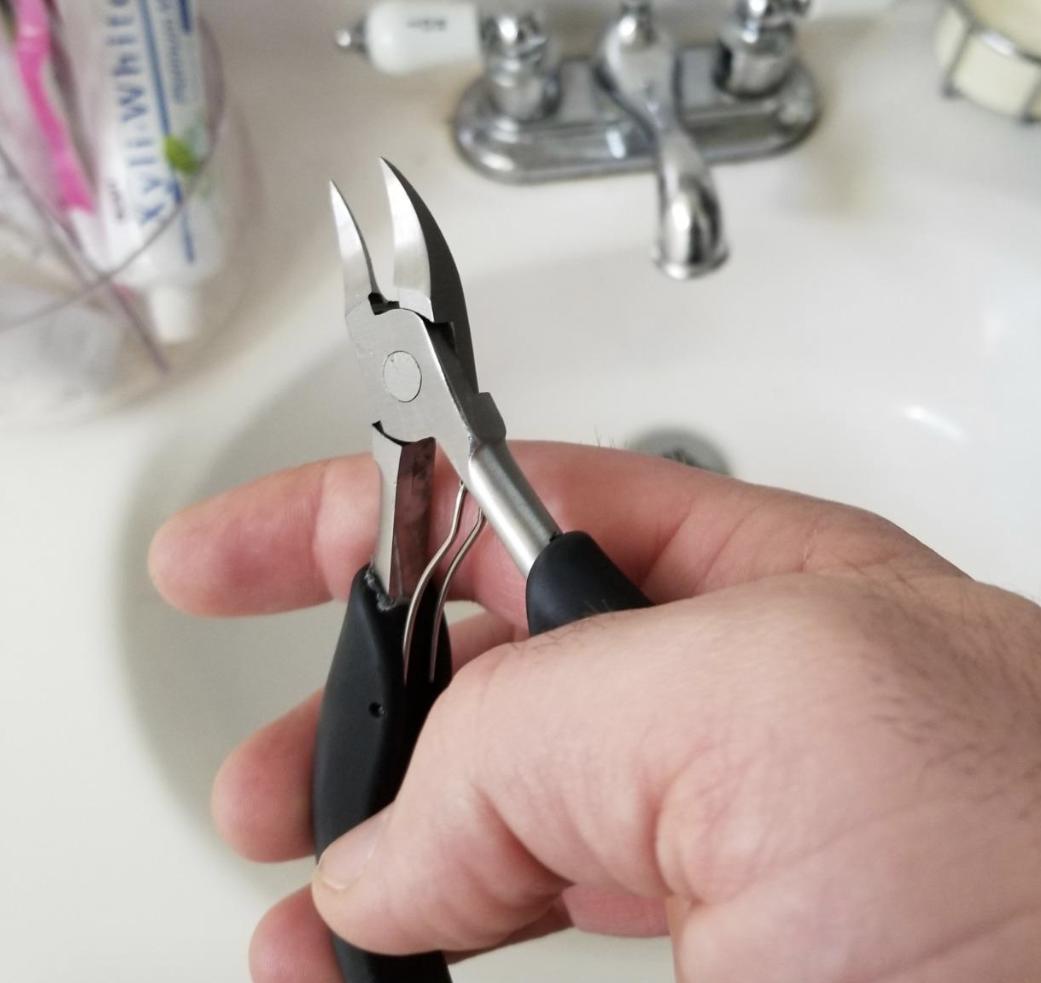 Reviewer holding up the small plier-shaped toenail clippers with pointed edges 