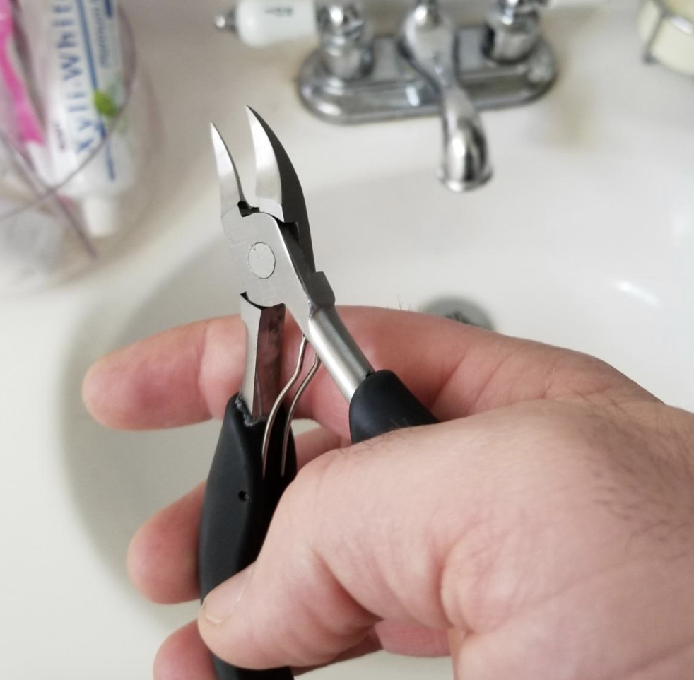 Reviewer holding up the small plier-shaped toenail clippers with pointed edges 