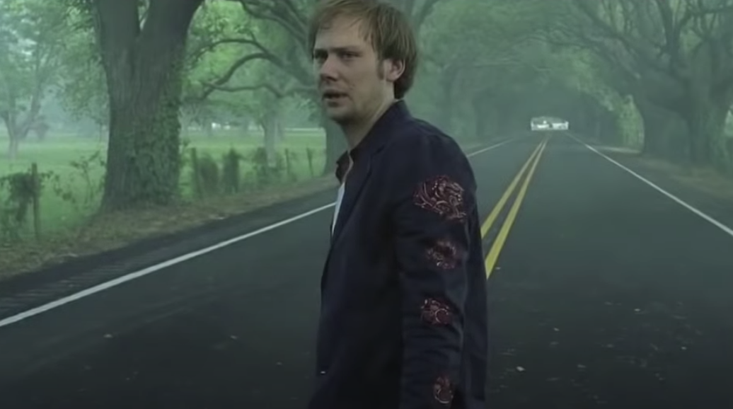 Jimmi Simpson standing in the middle of a road surrounded by trees as Phineus