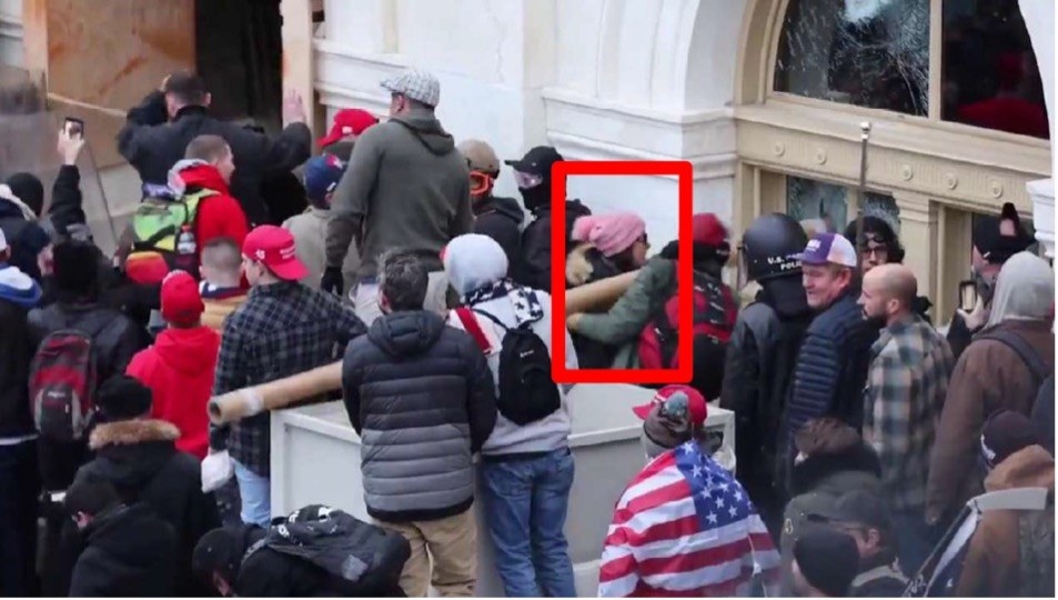 A woman in a pink hat and others ramming a window at the Capitol