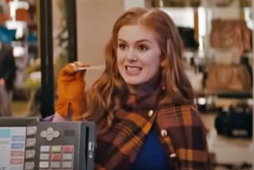 Isla Fisher holding up a credit card at a store checkout as Rebecca