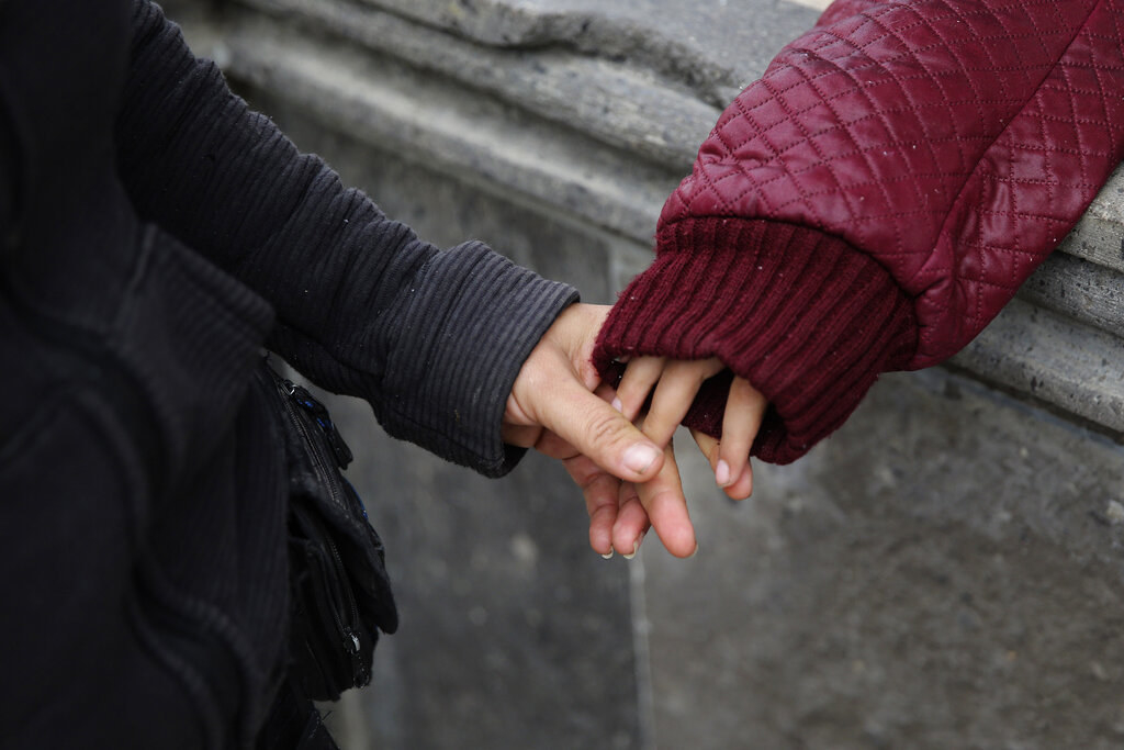 An adult&#x27;s hand holds the fingers of a child&#x27;s hand