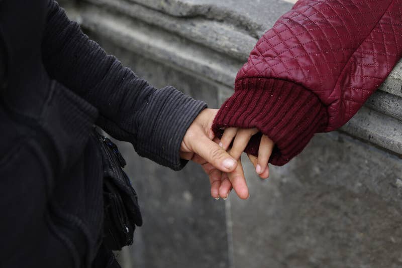 An adult's hand holds the fingers of a child's hand