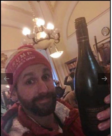 Riddle wears a Trump and holds a wine bottle up to the camera in the Capitol