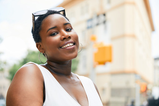 A smiling woman wearing sunglasses stands on a city street.