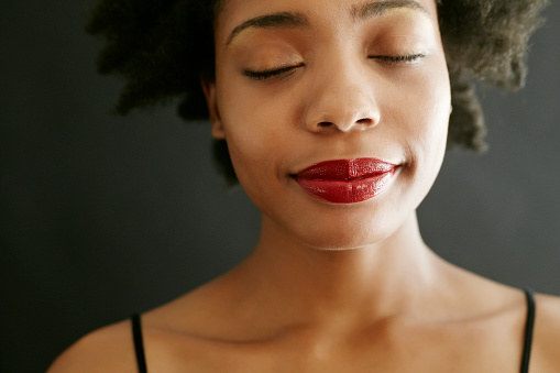 Close-up on a woman with red lipstick, radiant skin; her eyes closed.