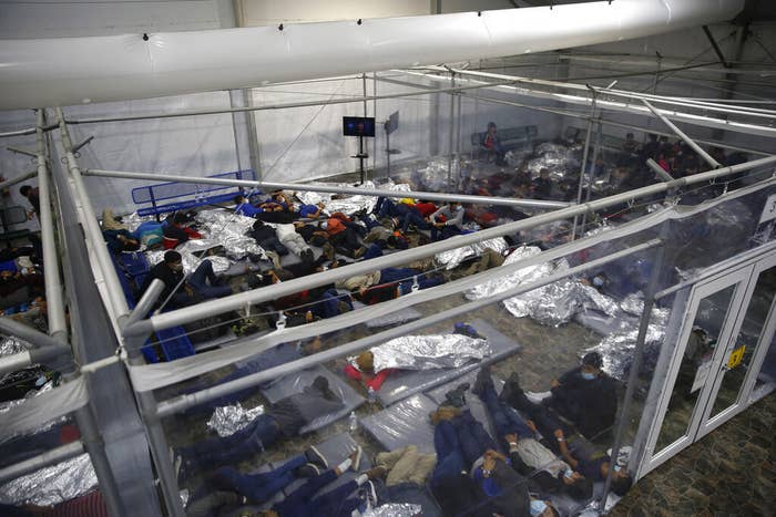 An overhead view shows dozens of people in a small room, many of them lying under emergency blankets