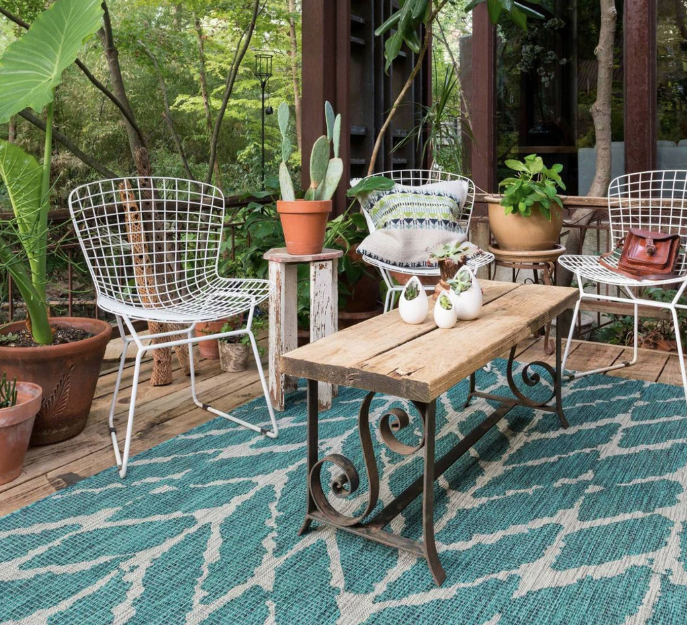 teal and white patterned outdoor rug below a wooden table and white iron chairs