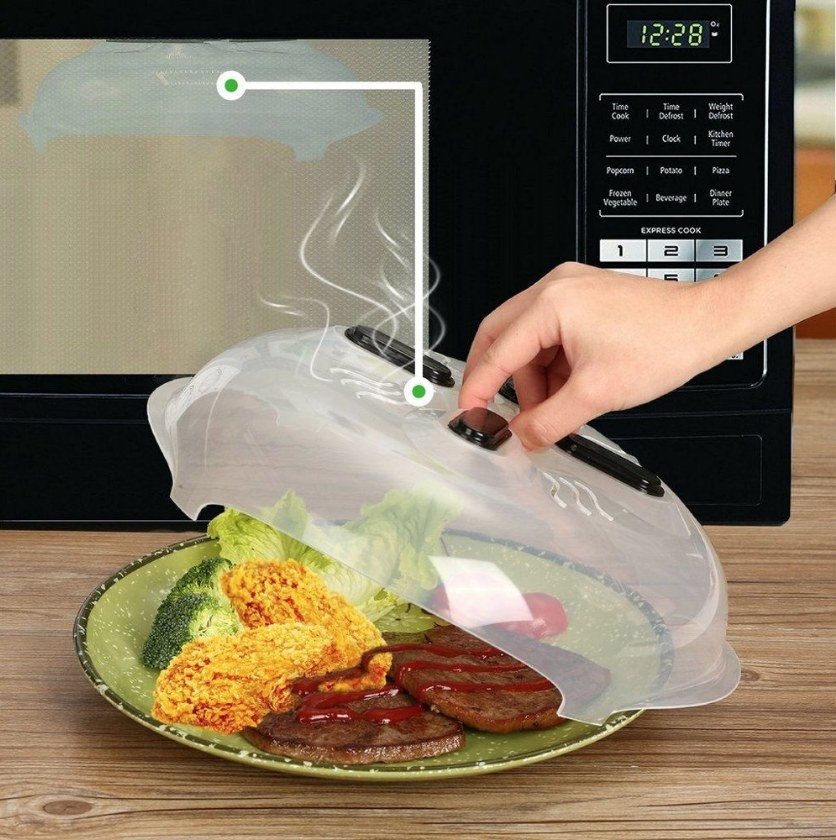 A microwave splatter lid with steam vents and microwave safe magnets being held up by a models hand displaying a meal underneath