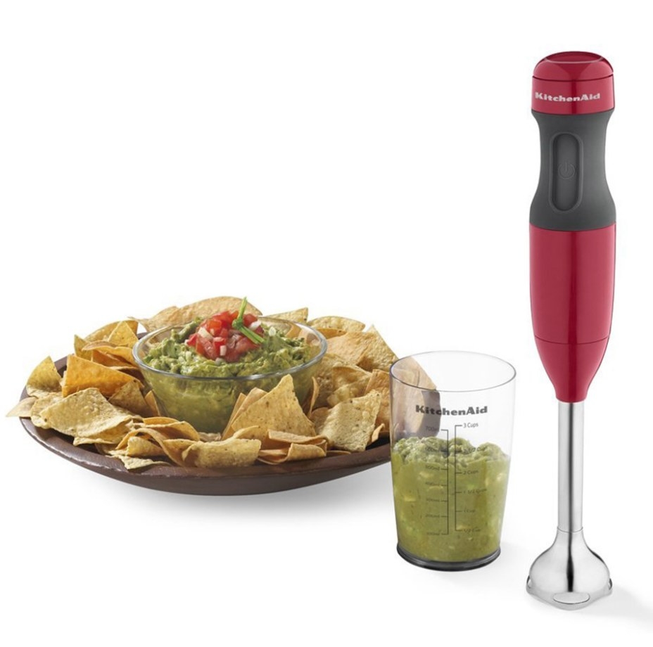 A red and black two-speed hand-hand immersion blender next to a cup of guacamole and a plate of chips