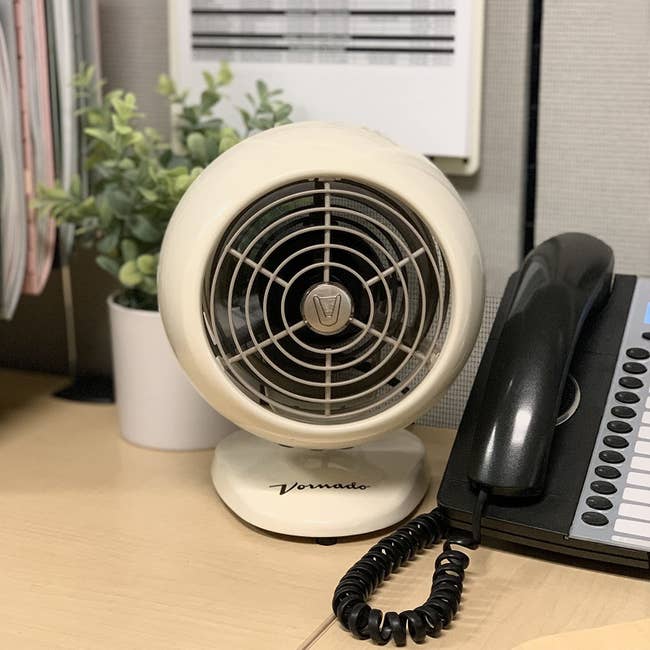 reviewer image of the vintage white vornado personal fan with a classic base on a desk next to an office phone